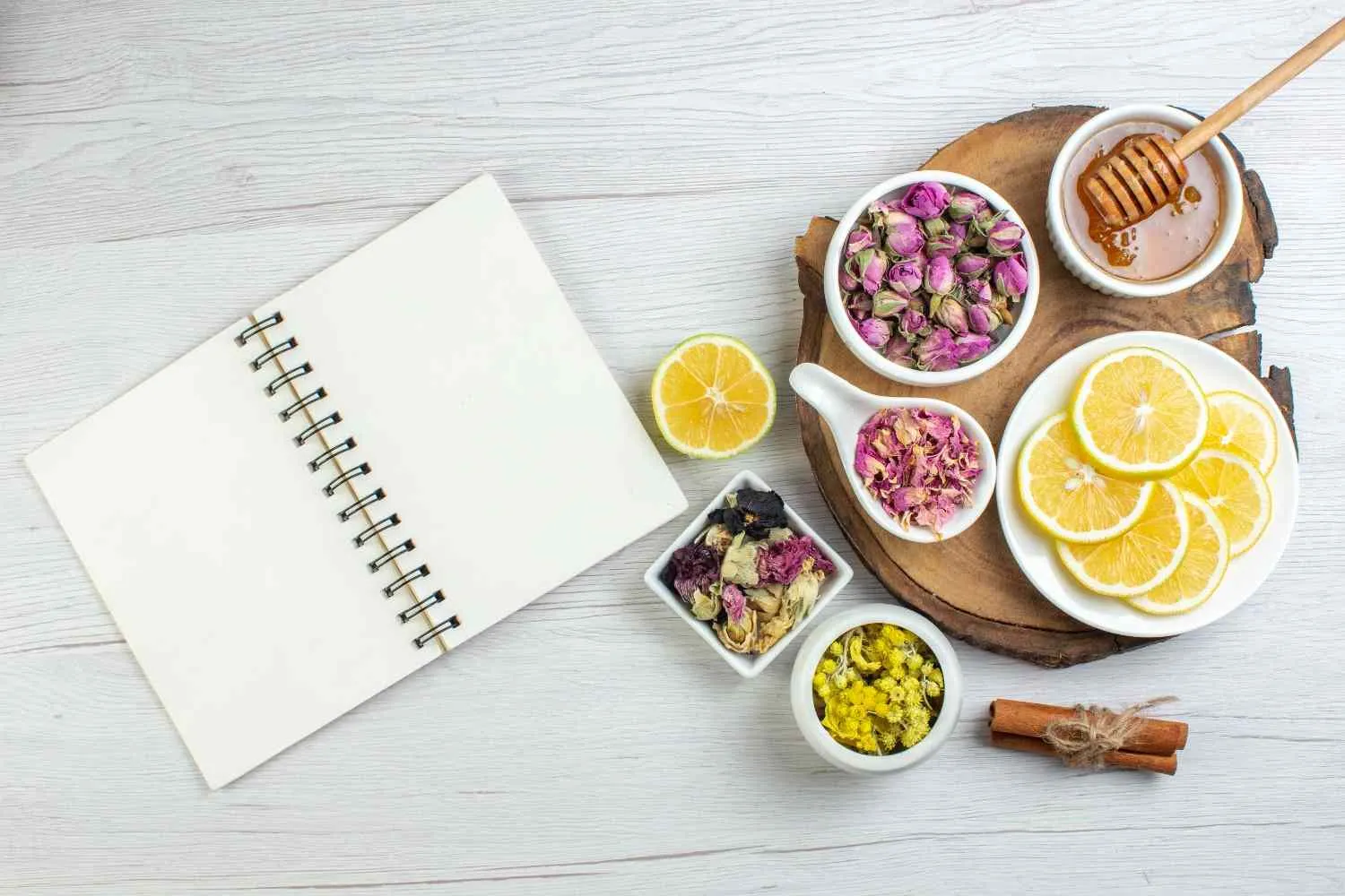 An open notebook beside lemon slices, dried flowers, honey and cinnamon